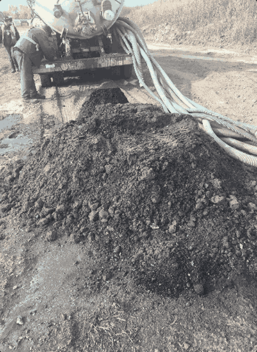 Vacuum truck pumping sewage sludge roadside